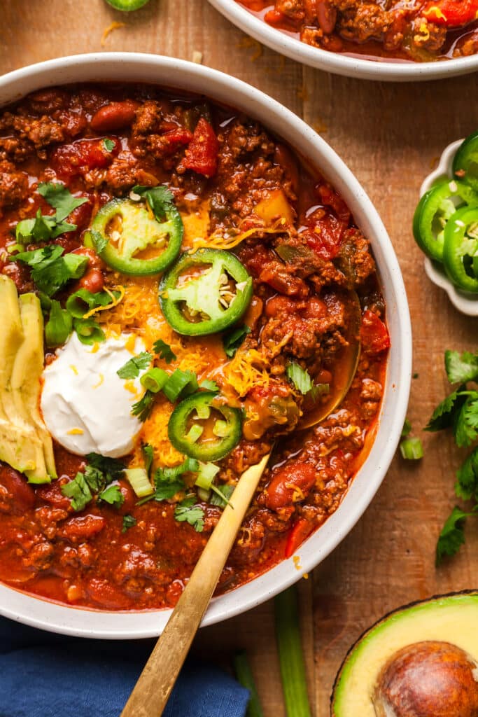 pcos friendly chili in a bowl topped with avocado, jalapenos, cheese, and sour cream.