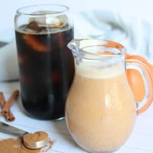 homemade pumpkin spice creamer in a small glass pitcher next to an iced coffee in a glass.