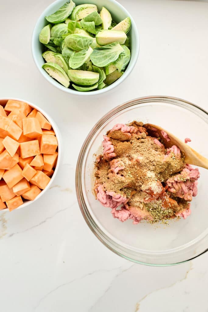overhead process shot of chopped sweet potatoes and brussels sprouts in bowls, and raw ground turkey and spices in a bowl.