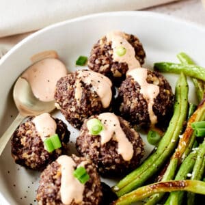 meatballs with a spicy sauce drizzled on top with green beans in a white bowl.