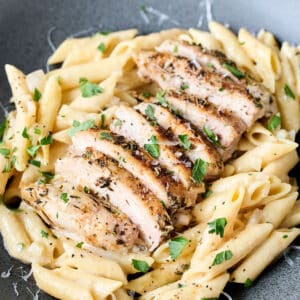 sliced chicken thighs on top of penne pasta with fresh parsley on top.