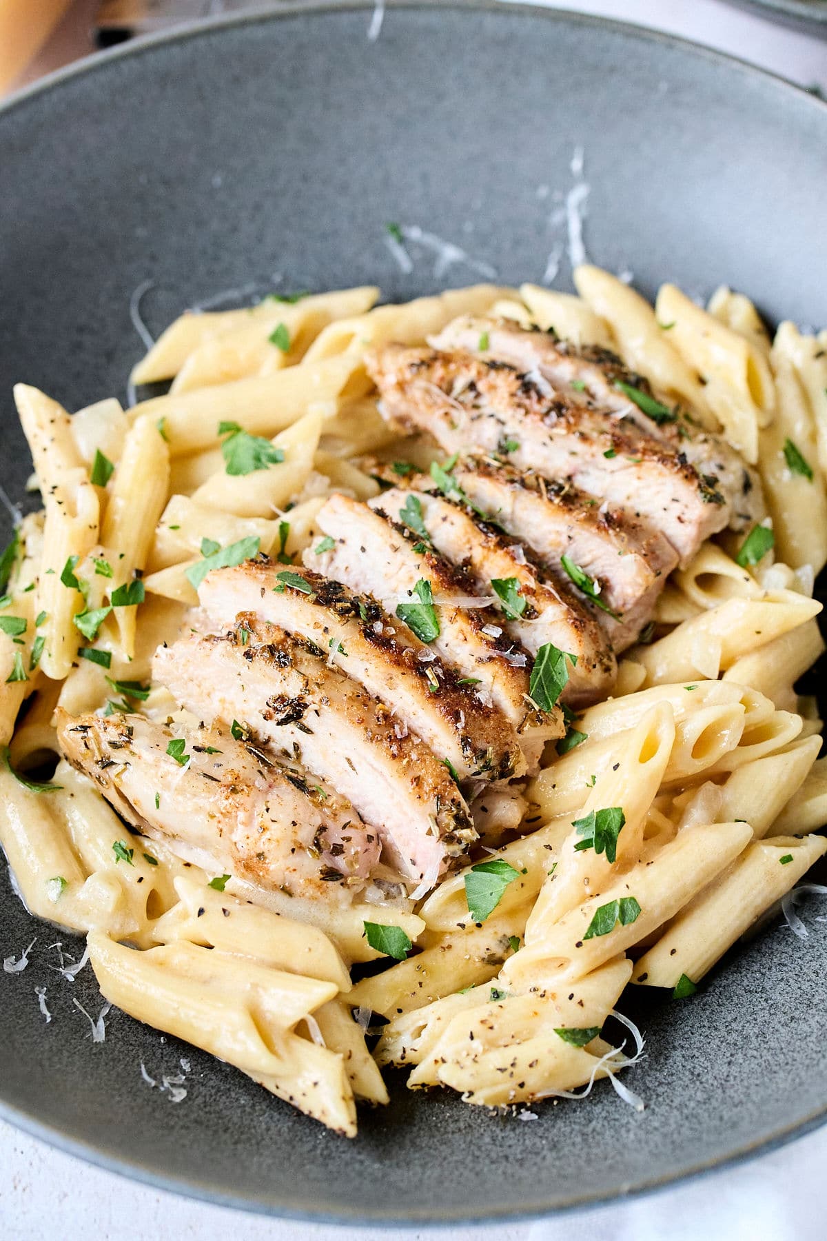 sliced chicken thighs on top of penne pasta with fresh parsley on top.