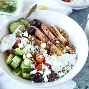 greek chicken quinoa bowl with tzatziki sauce in a white bowl with spoon.