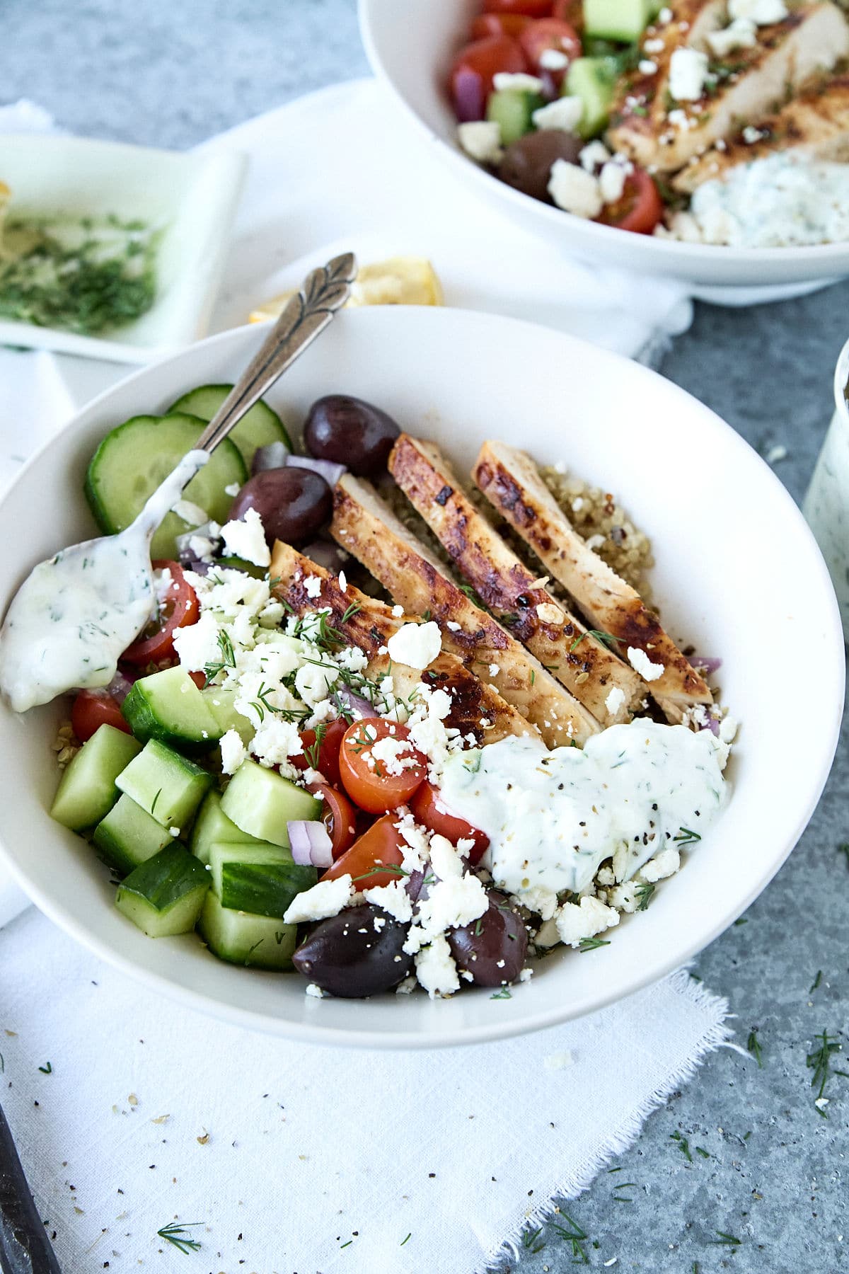 greek chicken quinoa bowl with tzatziki sauce in a white bowl with spoon.