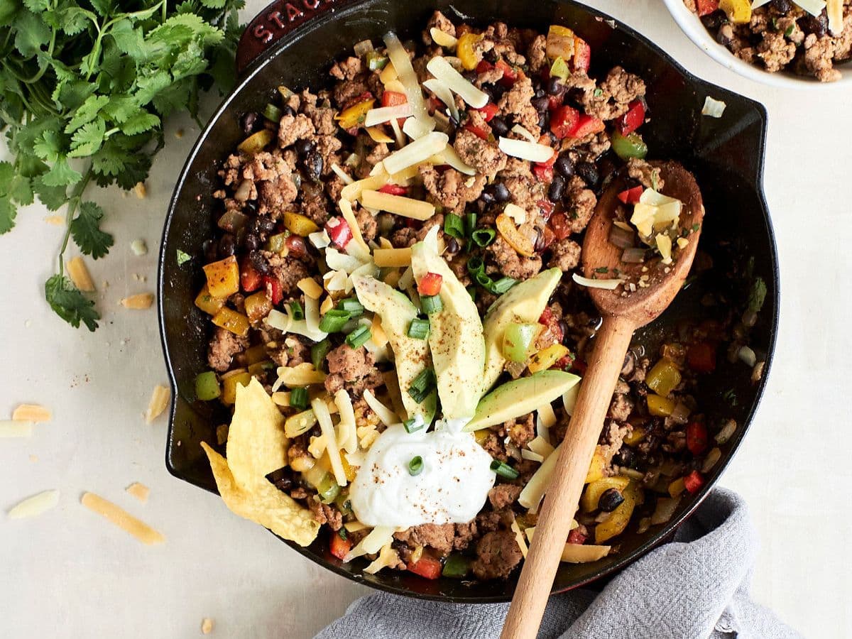 overhead shot of a ground turkey taco recipe in a black skillet with a wooden spoon in it.