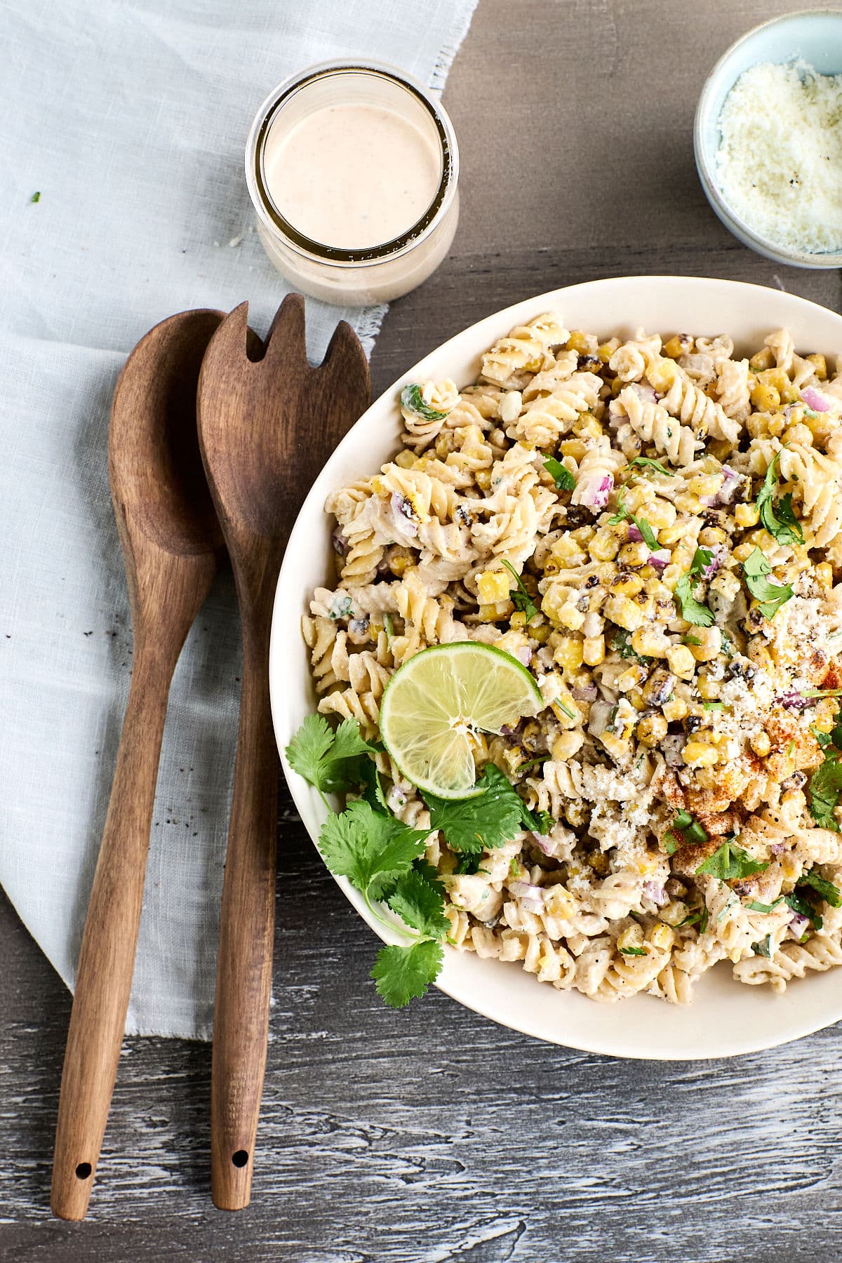 elote pasta salad on a plate with wooden serving utensils and dressing next to it.