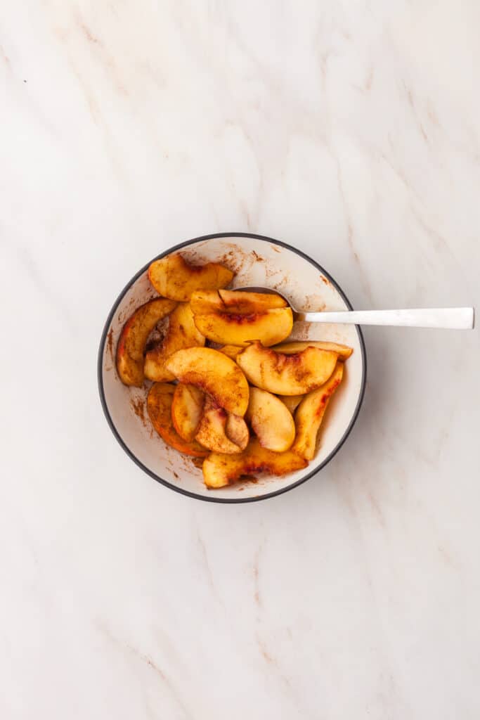peach slices in a bowl mixed with cinnamon, lemon juice and maple syrup.