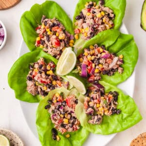 mexican tuna salad scooped onto lettuce wraps on a plate with lime wedges decorative.