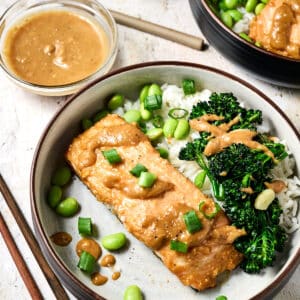 miso ginger salmon on a plate with rice and broccolini topped with edamame and green onions.