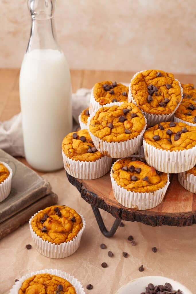 stacked cottage cheese pumpkin muffins on wooden platter with bottle of milk behind.