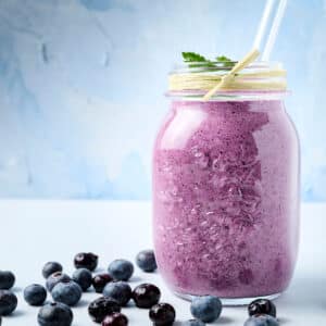 blueberry raspberry smoothie in a mason jar with a straw; blueberries on counter too.