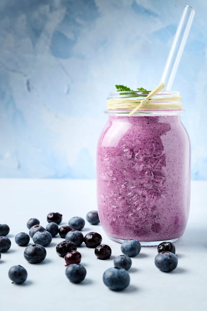 blueberry raspberry smoothie in a mason jar with a straw; blueberries on counter too.
