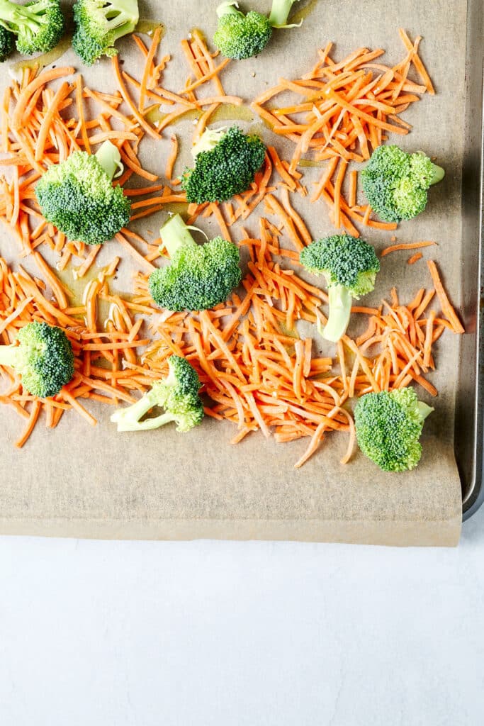 shredded carrots and broccoli on a parchment lined baking sheet.