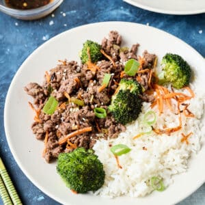 korean ground beef bulgogi with white rice and veggies on a white plate.