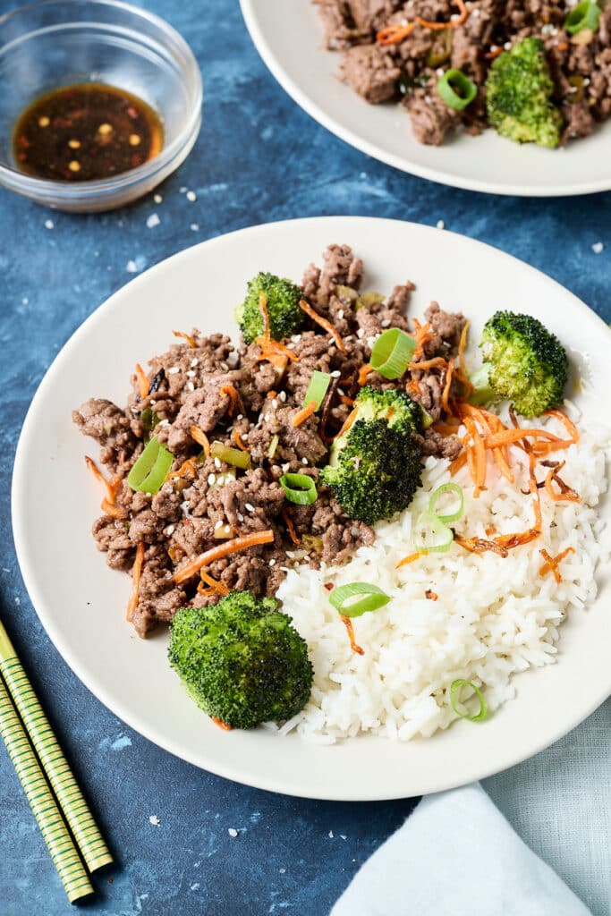 korean ground beef bulgogi with white rice and veggies on a white plate.