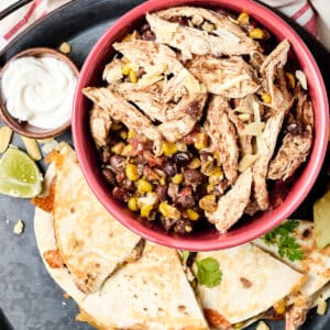 shredded southwest chicken, black beans, and corn in red bowl with quesadilla next to it.