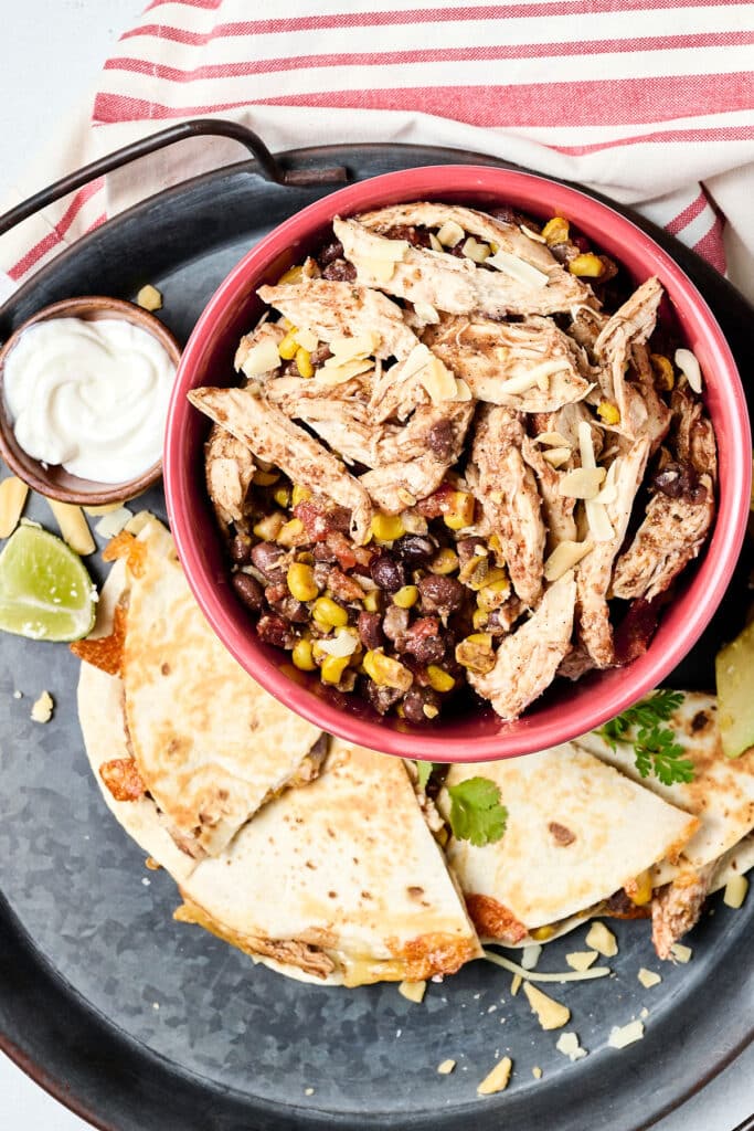shredded southwest chicken, black beans, and corn in red bowl with quesadilla next to it.