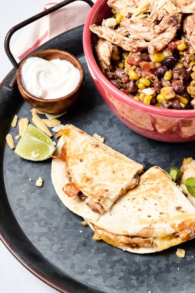 shredded southwest chicken, black beans, and corn in red bowl with quesadilla next to it.
