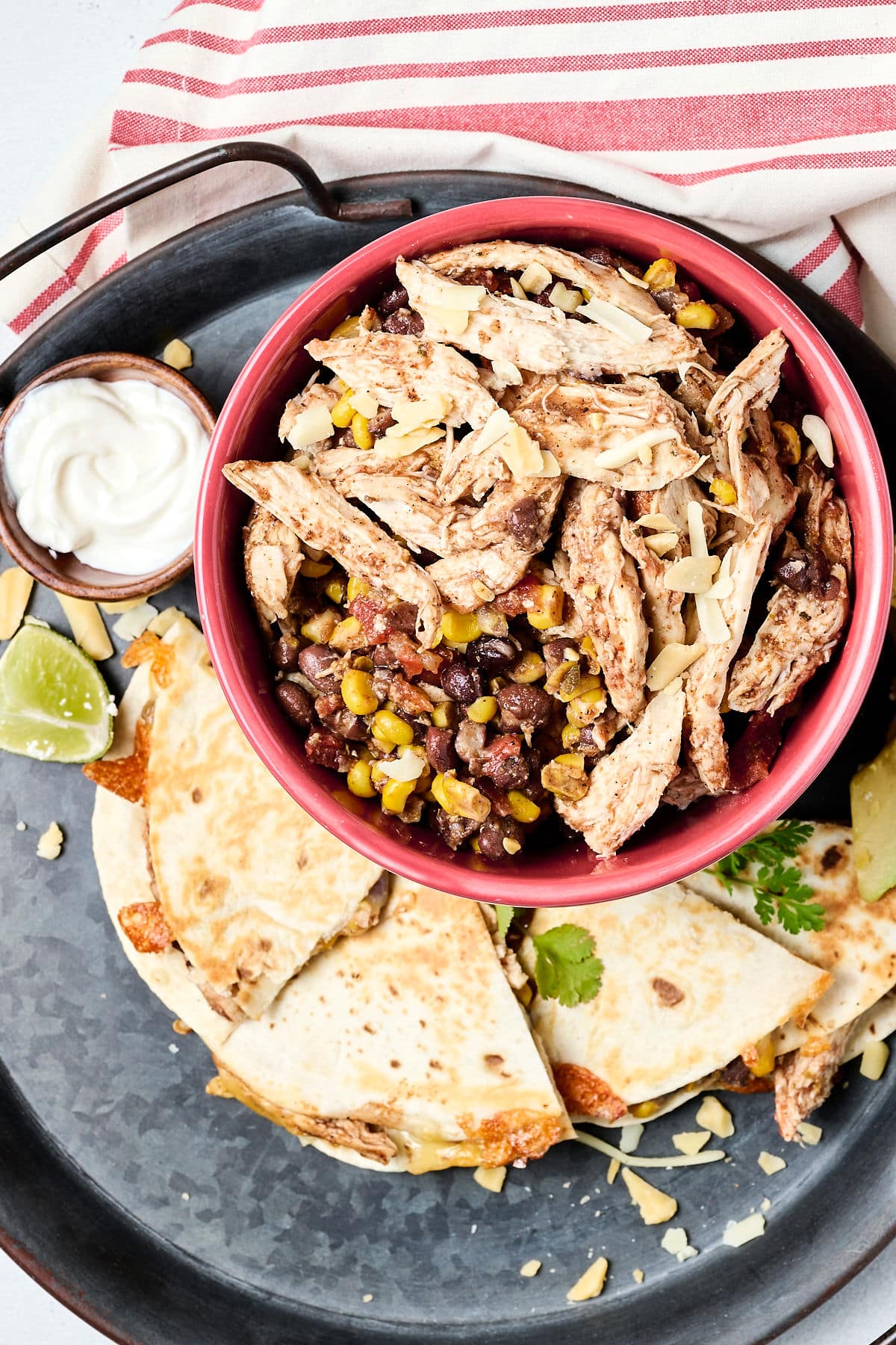 shredded southwest chicken, black beans, and corn in red bowl with quesadilla next to it.