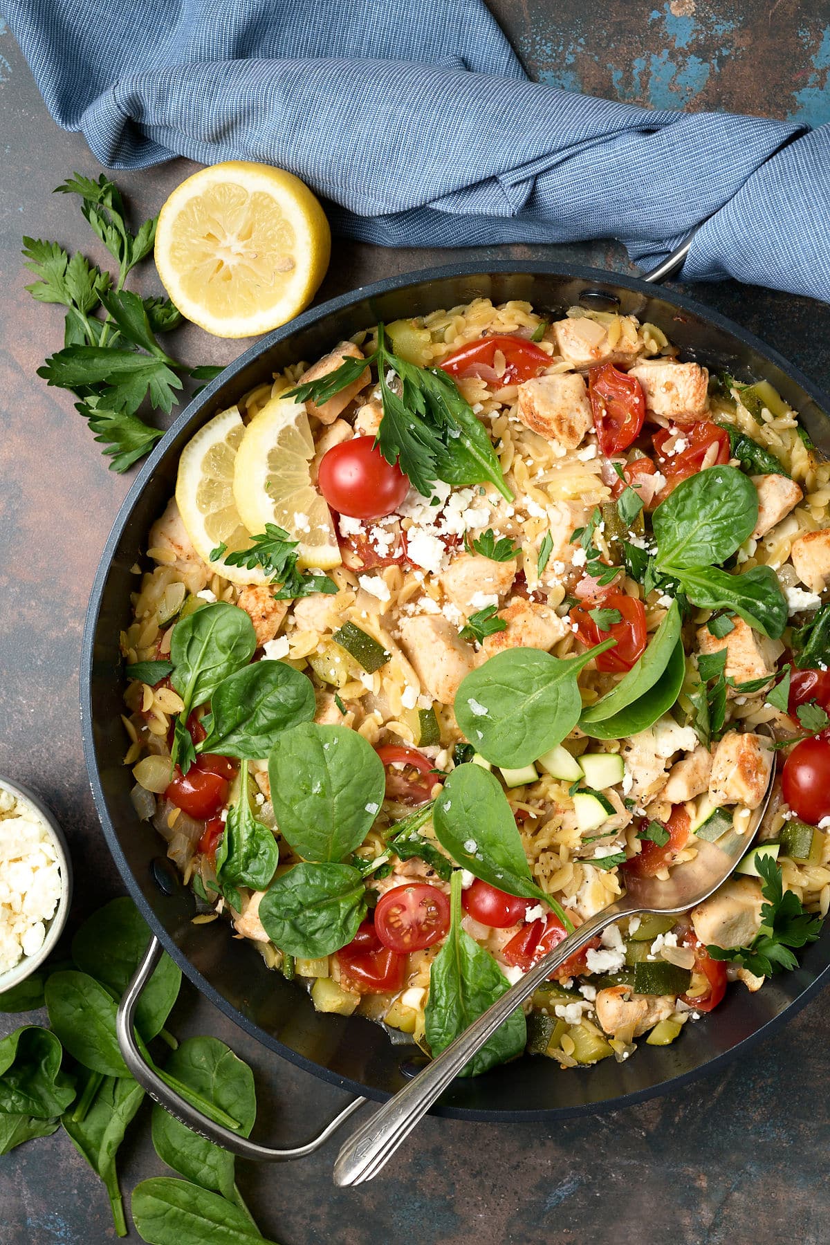 chicken orzo bake in a skillet with fresh herbs and lemon wedges.