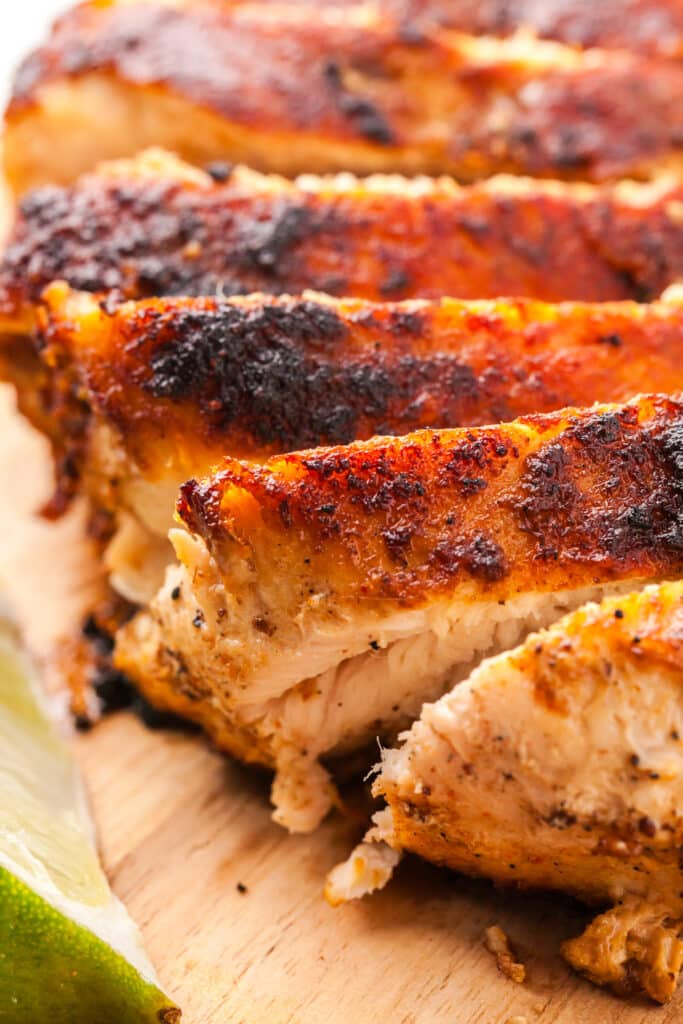 seasoned chicken breast sliced on a wooden cutting board.