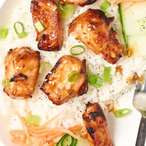 air fryer teriyaki salmon bites over a bed of rice with cucumber ribbons and shredded carrots.