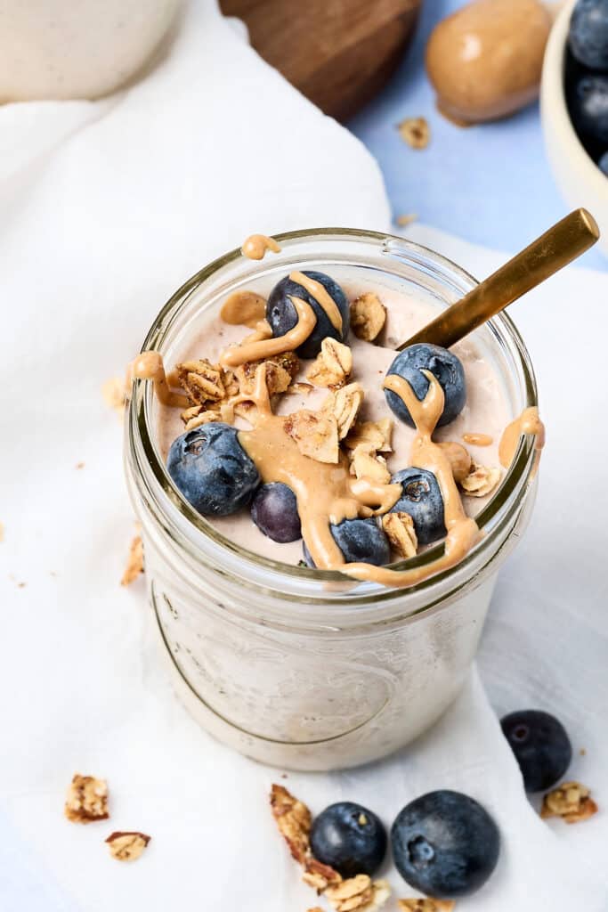blended overnight oats in a mason jar with blueberries and nut butter drizzle.
