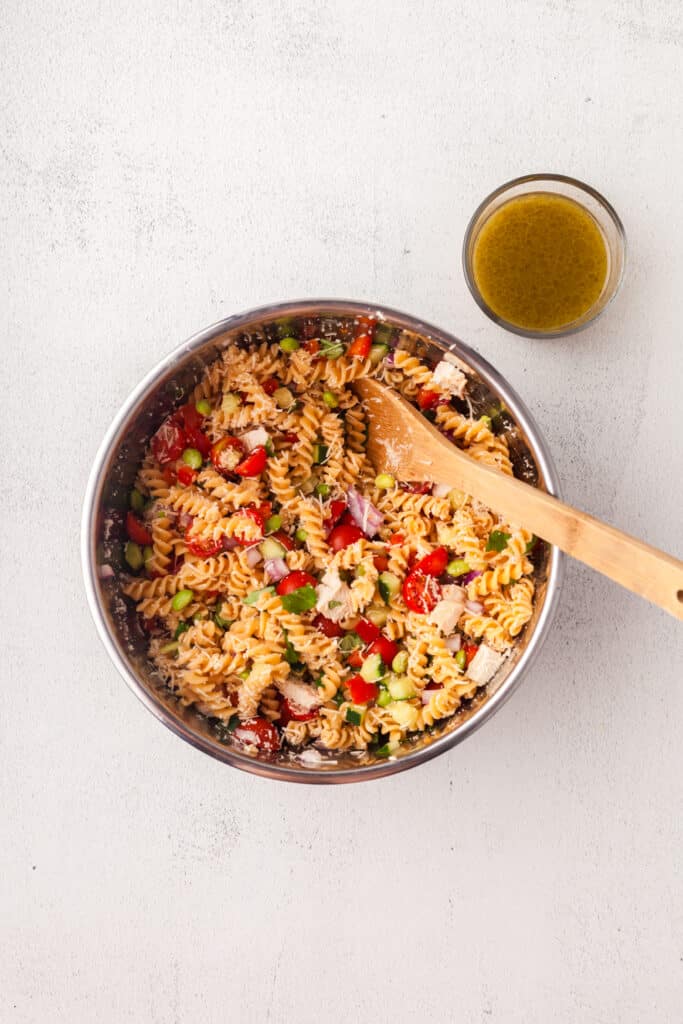 making a high protein pasta salad in a large mixing bowl with side dish of dressing.