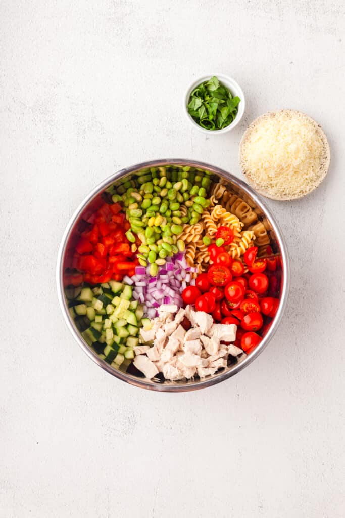 adding ingredients for a high protein pasta salad to a stainless steel mixing bowl.