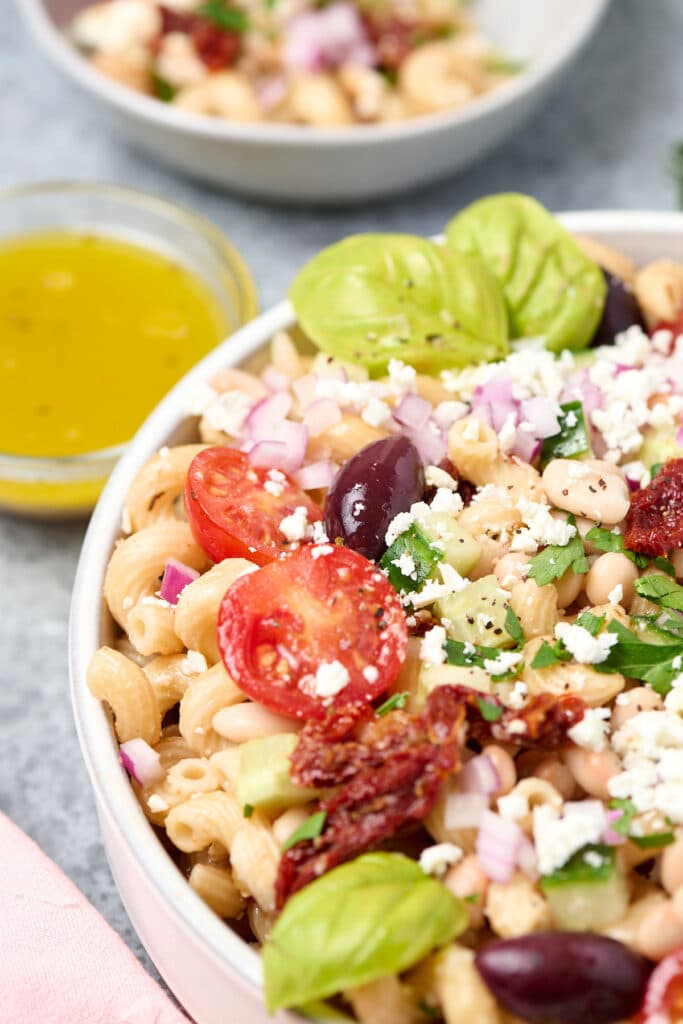 close up view of a mediterranean bean pasta salad on a white plate.