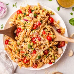 high protein pasta salad on a large white plate with wooden serving utensils.