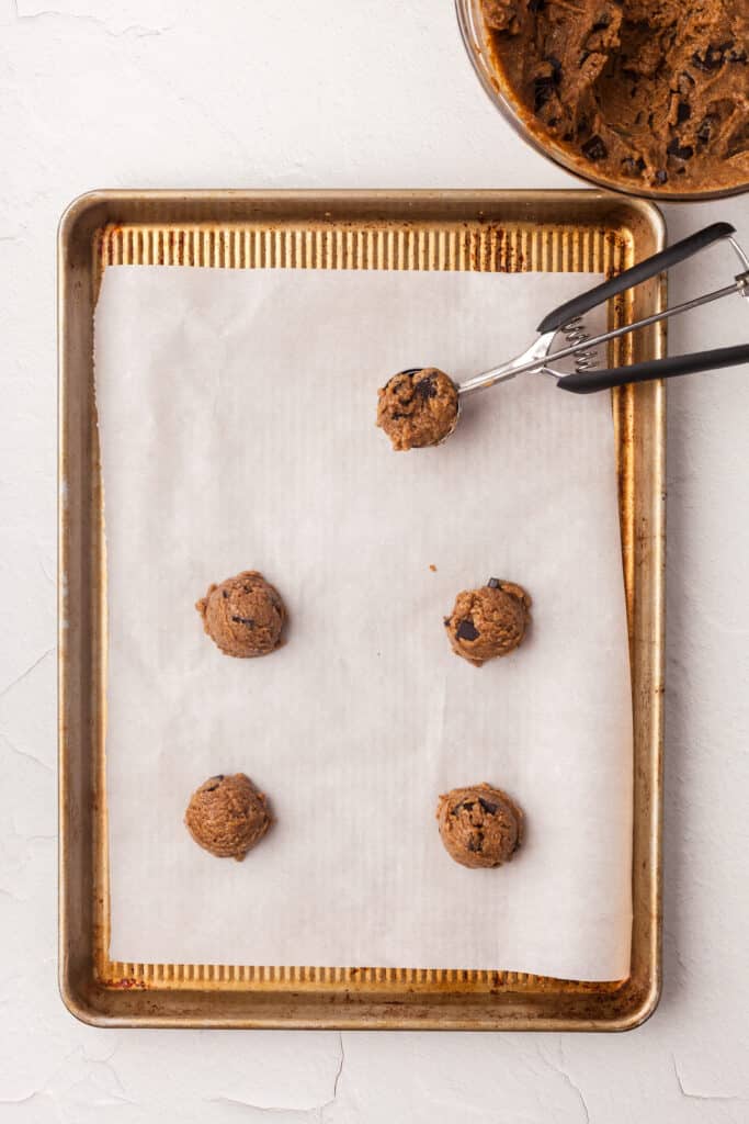 cookie scoop with cookie dough being put onto parchment lined baking sheet.