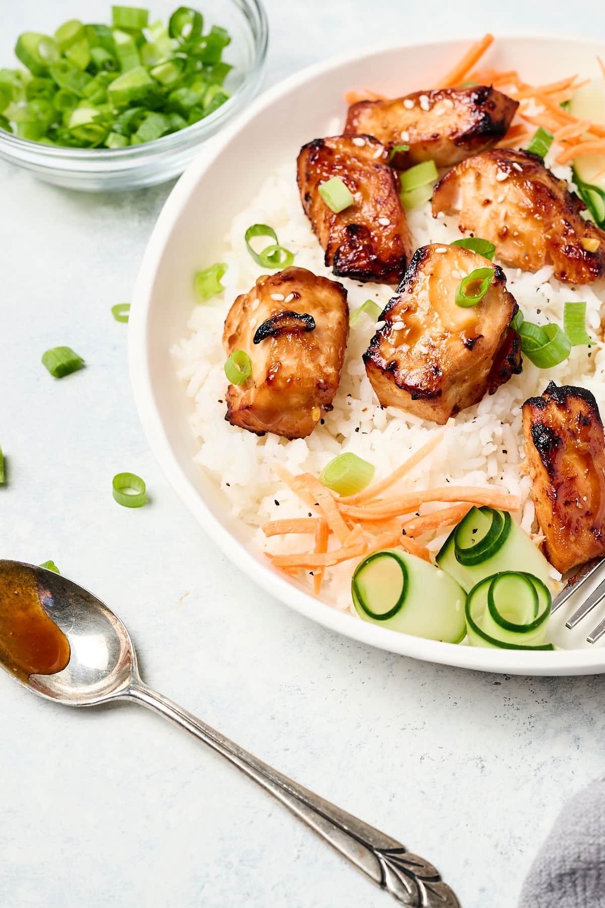 teriyaki salmon bites on a white plate with white rice, cucumber ribbons, and shredded carrots.