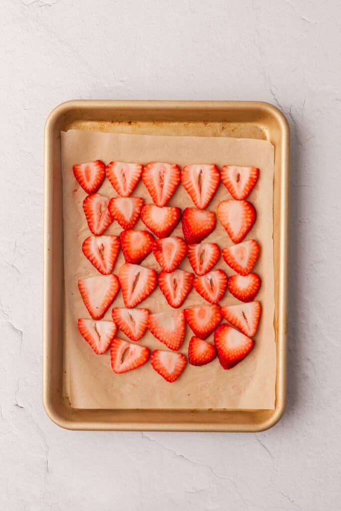 strawberry slices arranged on a parchment lined baking sheet.