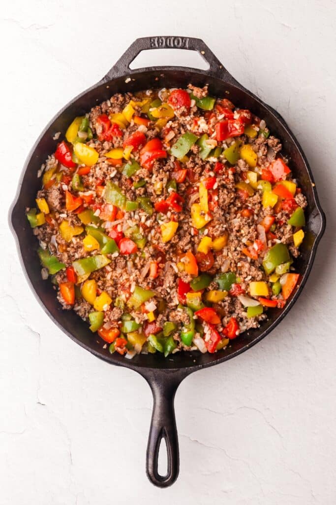 ground beef and bell peppers in cast iron skillet.