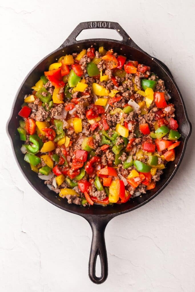 ground beef and bell peppers in cast iron skillet.