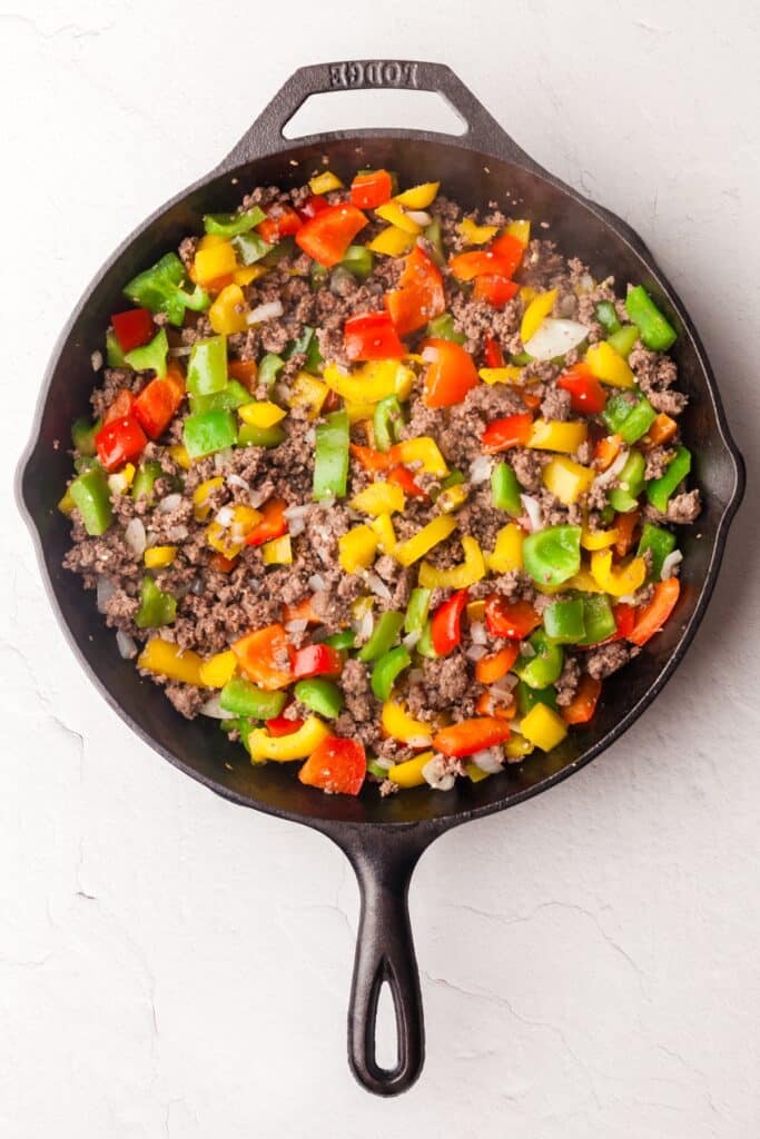 ground beef and bell peppers in cast iron skillet.