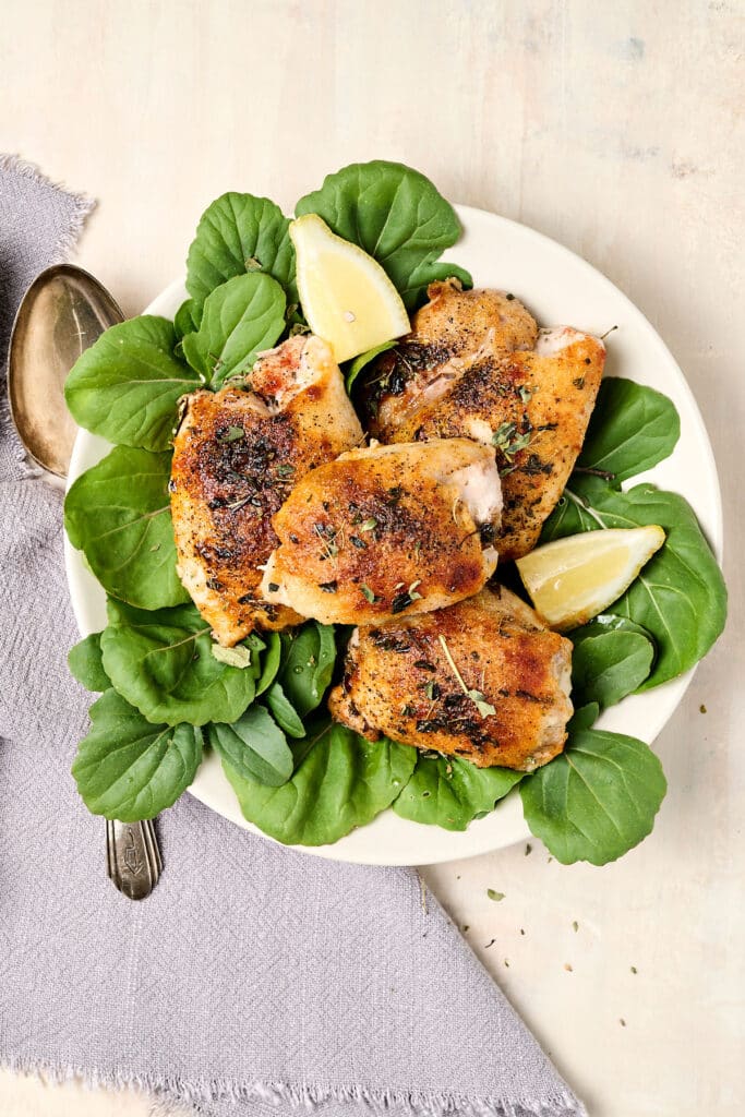 oven baked boneless skinless chicken thighs on a bed of leafy greens on a white plate.