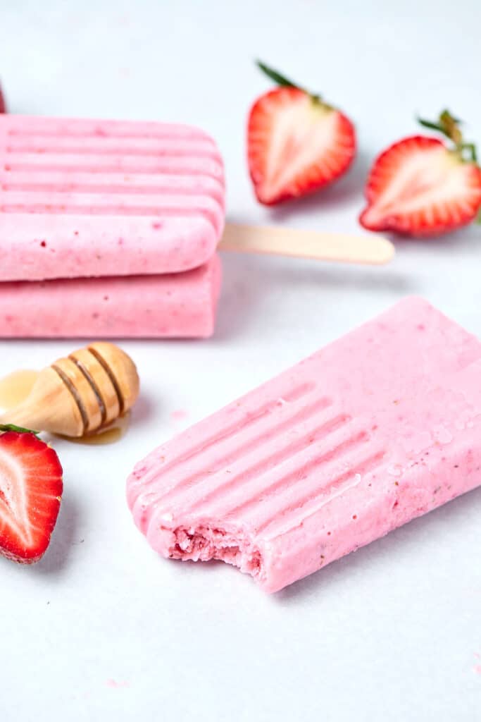 strawberry protein popsicles on a gray countertop with strawberries and honey.