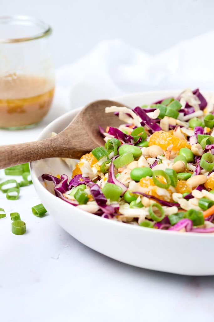 crunchy asian salad with mandarin oranges and edamame in a bowl with wooden spoon.