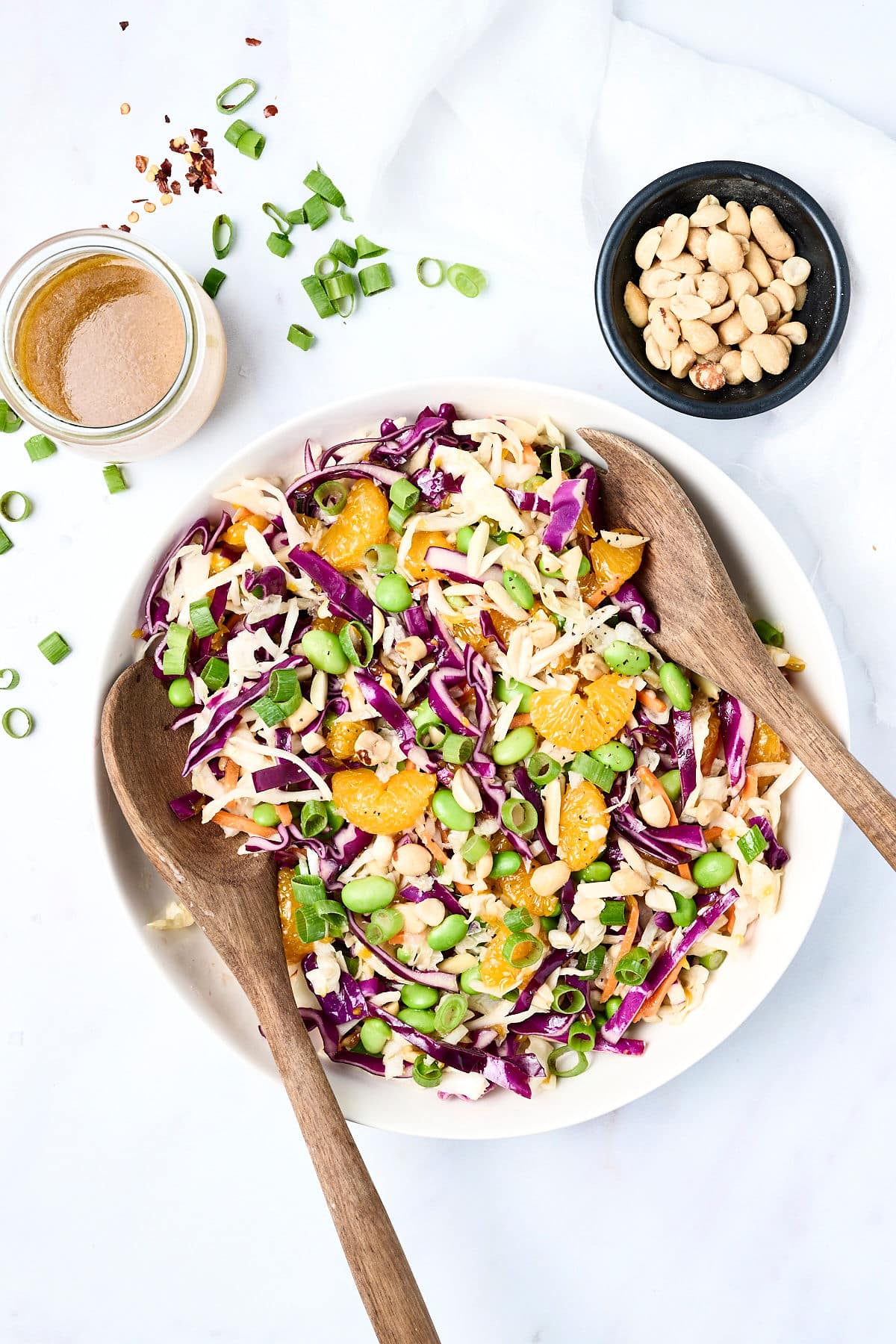 crunchy asian salad with mandarin oranges and edamame in a bowl with wooden spoons.