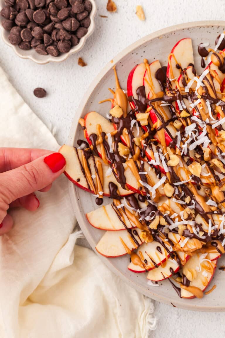 hand pulling an apple slice out of apple nachos platter.