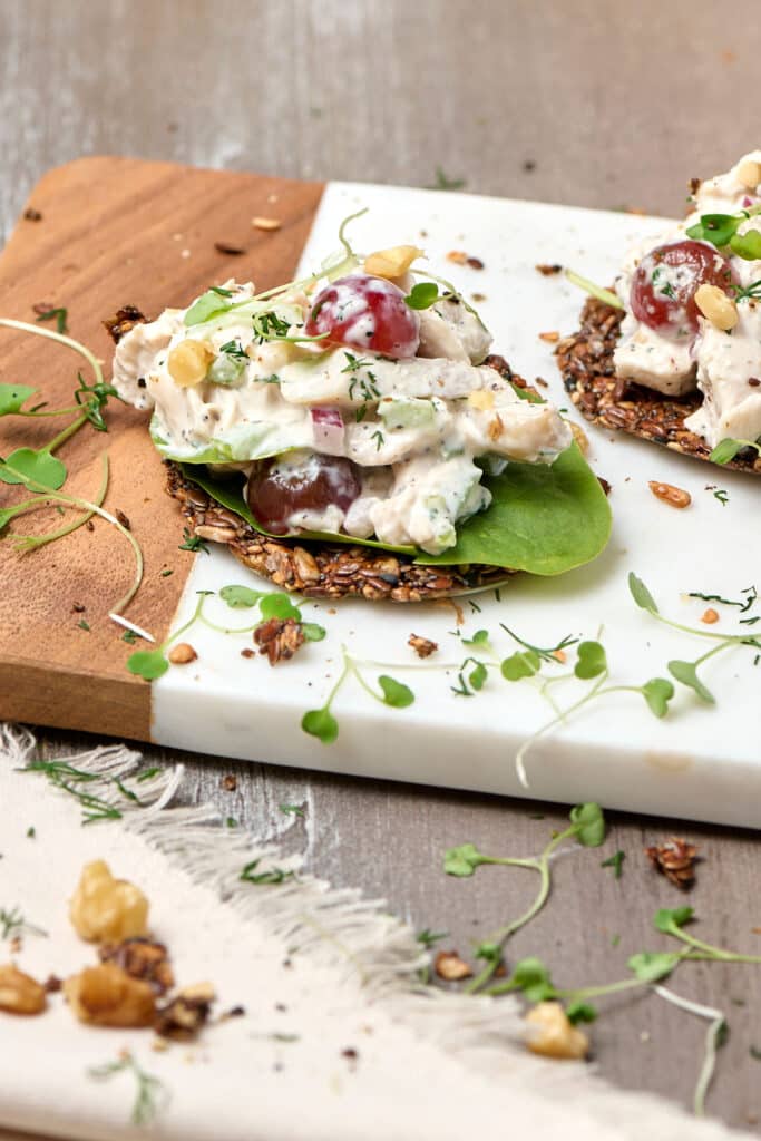 pcos chicken salad on seed crackers on a cutting board.