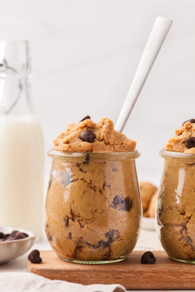 chickpea cookie dough in a glass jar with a spoon; milk bottle in the background.