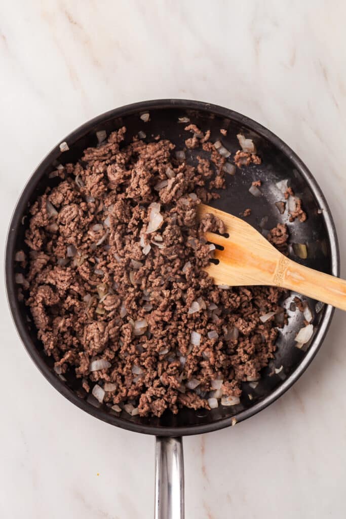 ground beef and onions in a saute pan with wooden spoon.