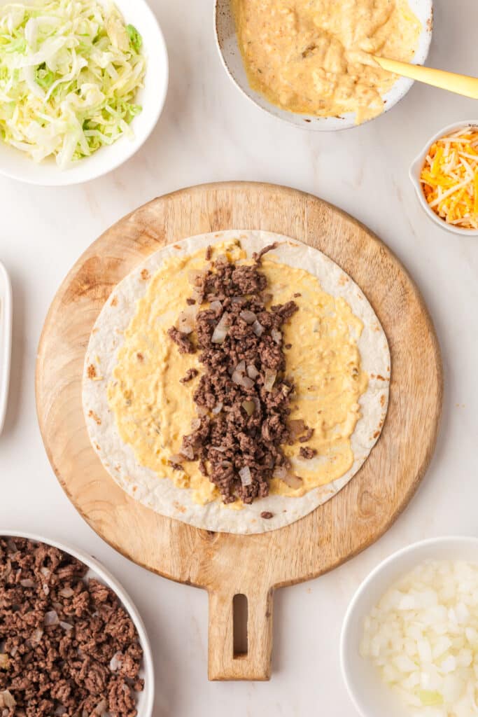 open tortilla with big mac sauce spread on it and ground beef.