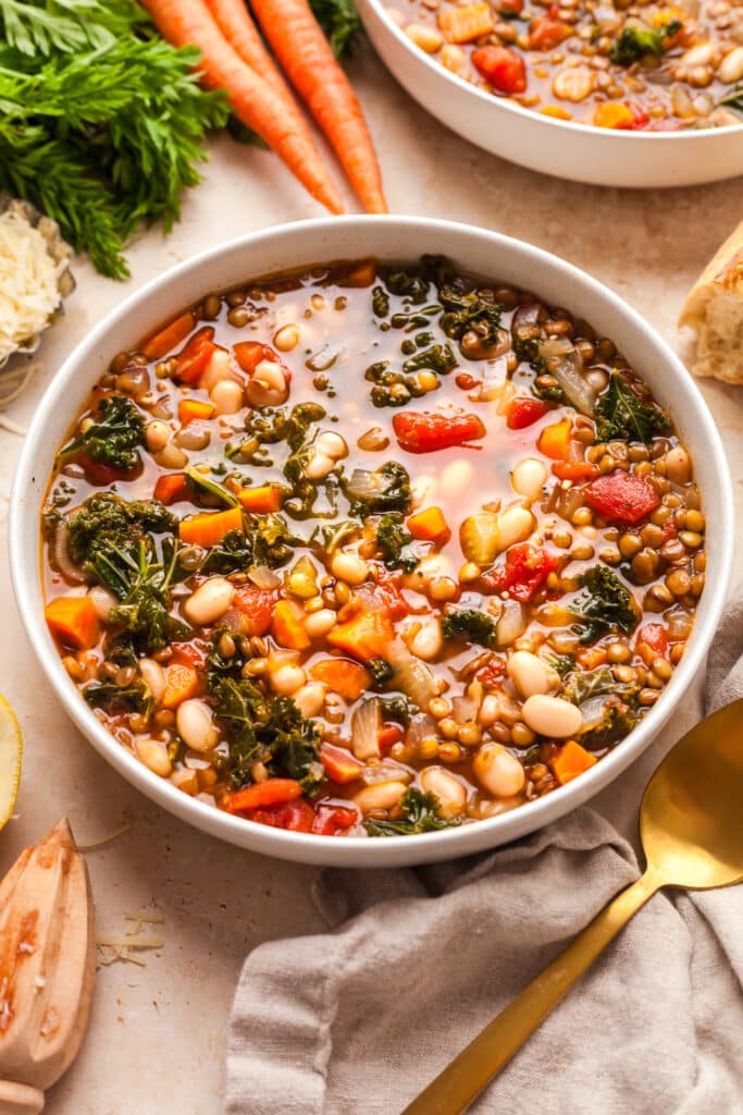 white bowl with lentil and white bean soup; additional ingredients surround the bowl.