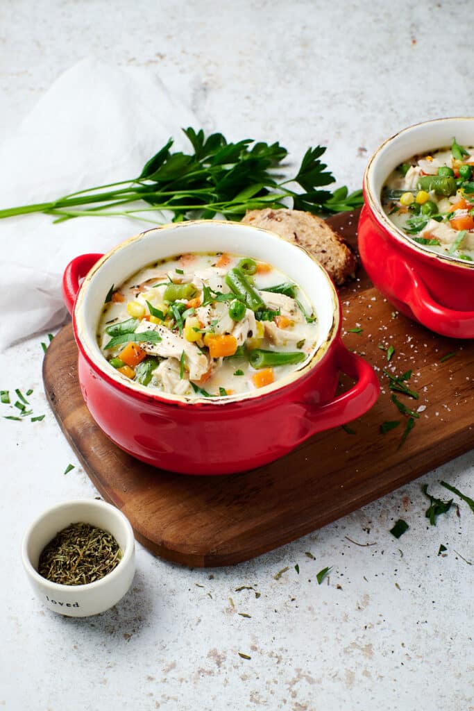 chicken pot pie in a red bowl on top of a wooden cutting board.