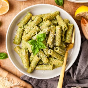 protein pesto pasta in white bowl with gold spoon inserted on wooden countertop.