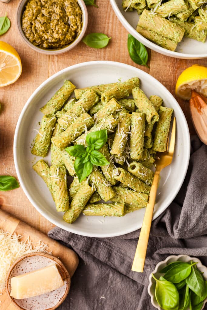 protein pesto pasta in white bowl with gold spoon inserted on wooden countertop.